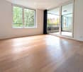 Empty room with light wooden flooring, large windows, and sliding glass doors leading to a balcony.