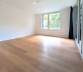 Empty room with light wooden flooring, white walls, and large windows allowing natural light. No furniture or equipment is present.