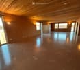 Empty room with bare walls and polished concrete floor, wooden ceiling, large windows, and sliding glass door.