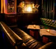 A stylish lounge area with leather sofas, small tables with candles, decorative vases, and a mirror behind the bar.
