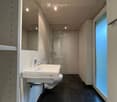Modern bathroom with white sink, large mirror, toilet, and glass-enclosed shower. Dark tiled floor and white walls.