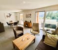 Modern living room with a sofa, coffee table, chairs, dining table, and a view through large windows.