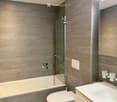 Modern bathroom with grey wood-paneled walls, a bathtub, toilet, sink, and a glass-enclosed shower area.