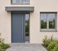 Modern house entrance with a grey front door, large windows, and small garden area with shrubs.