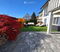 Well-maintained garden with artificial grass, patio furniture including a sofa, coffee table, and chairs, surrounded by colorful foliage and a modern house.