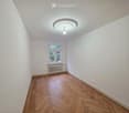 Empty room with wooden herringbone flooring, white walls, a single window with a radiator below, and a ceiling light fixture.