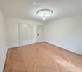 Empty room with light-colored walls, wooden herringbone flooring, and a decorative ceiling light fixture.