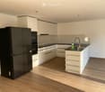 Modern kitchen with white cabinets, black countertops, and a central island. Features a black refrigerator, oven, and a sink with a modern faucet.
