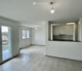 Empty room with tiled floor, white walls, and a small kitchen area with cabinets and a countertop. Features large windows and a sliding glass door leading to a balcony.