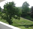 Balcony overlooking a green garden with trees and a road beyond.