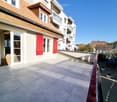 Balcony with tiled flooring, red railing, and view of neighboring buildings and parked cars.