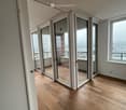 Empty room with wooden flooring, large glass sliding doors leading to a balcony, and white walls.