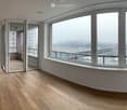 Empty room with wooden flooring, large windows, and a sliding glass door leading to a balcony.