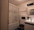 Bathroom with a shower enclosure, toilet, sink, and mirror. Hair dryer and soap dispenser are mounted on the wall.