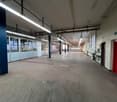 Industrial building, wide open space, long hallway, fluorescent lights, concrete floor, several windows, red doors
