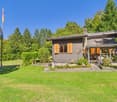 Wooden house, grey exterior, orange shutters, covered porch, green lawn, trees, flag pole