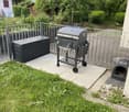 BBQ grill and storage box on paved area, metal fence, grassy area, and a pet house in gravel