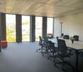 empty meeting room with large windows, carpeted floor, long tables, office chairs, plants