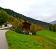 2 houses in a mountain area, surrounded by trees, with a road and open fields