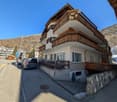 4 story building, wooden balconies, white exterior, stone retaining wall, mountain backdrop