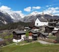 Traditional alpine village with wooden chalets, set against the backdrop of snowy mountains, one with a steeple.