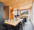 Spacious dining area with a large wooden table and black chairs, a fireplace, and large windows overlooking a balcony or terrace with a scenic mountain view