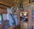 Rustic wooden cabin interior with a fireplace, kitchen area, and sleeping area visible. The cabin has a cozy, outdoorsy feel with mounted antlers and other decor.
