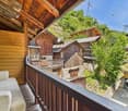 Wooden cabin-style houses with balconies, surrounded by lush greenery and trees. The houses have a rustic, mountain-like appearance.
