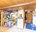 The image shows a cluttered utility room or storage space with a wooden ceiling and walls. It contains various shelves, cabinets, and storage containers filled with household items, appliances, and other miscellaneous objects. A washing machine is visible