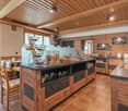Rustic kitchen with wooden walls and ceiling, large central island with drawers, black countertops, and various kitchen appliances and serving dishes on display