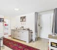 Open-plan studio apartment with hardwood flooring, white walls, a wooden cabinet with drawers, a fireplace, and a colorful patterned rug on the floor. The apartment also has a curtain-covered entryway and various decor items and artwork on the walls.