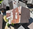 The image shows a bird's eye view of a residential area with multiple buildings. The buildings have a mix of red tile and gray roofs, and some have balconies or terraces visible. The buildings appear to be multi-story structures, and there are trees and g