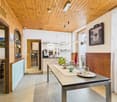 Dining area with wooden walls, dining table, and kitchen with appliances like a coffee machine and refrigerator