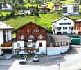 Apartment buildings, wooden facade, many windows, flags in front, car parking, green lawn, surrounding hills