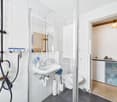 modern bathroom with walk-in shower, white tiles, sink, toilet, shelves, and a washing machine