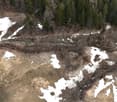 Aerial view of a garden with patches of snow, trees, and a small stream