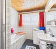 Bathroom with white bathtub, white sink, white washing machine, wooden ceiling, tiled walls, red curtains, and a mirror.