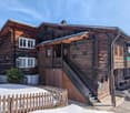 Traditional wooden chalet, steep roof, wooden exterior, multiple windows, wooden stairs, wooden fence