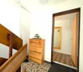 A hallway with wooden stairs, a wooden cabinet with drawers, a mirror, and a tiled floor.
