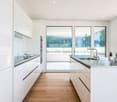 modern kitchen with white cabinets, wooden floor, granite countertops, stainless steel sink, large windows with view of the outside
