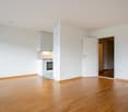 Large empty room, wooden floor, open kitchen with an oven, doorways leading to other rooms