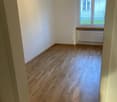 large empty room with wooden floors, white walls, single window