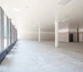 Large open floor plan with concrete flooring, white walls, and multiple columns supporting the ceiling. The space has large windows along one side, providing natural light. There are no visible furnishings or fixtures, indicating this is an unfinished or