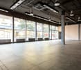 Large open commercial space with high ceilings, concrete floors, and large windows overlooking the exterior. The space has a modern, industrial design with exposed ductwork and lighting fixtures.
