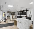 modern store with white walls, marble counter, glass doors, clothing racks, mannequins, monitor, wooden desk, black carpet