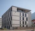 modern grey concrete building, 4 floors, windows, balconies, surrounded by mountains