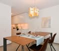 Dining table with chairs, wall painting, modern chandelier, kitchen in the background