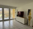 Spacious living room with large windows providing a scenic view, tiled flooring, a TV stand with a TV, and a decorative abstract art piece on the wall.