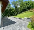 Stone patio, surrounded by grassy hillside, fenced area, outside table and chairs