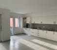 Spacious open-plan kitchen and living area, white cabinets, gray countertops, tiled flooring, large windows, and access to a balcony or terrace.